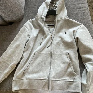 Ralph lauren zip hopdie - En helt ny grå Ralph lauren zip hoodie. Använd fåtal gånger så den är i nyskick. Inga fläckar eller skador.