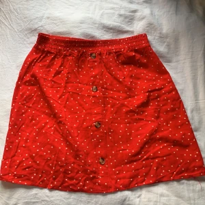 Röd prickig kjol - En kort och luftig sommar kjol som går att styla bra med andra plagg, den har bruna knappar i fram.
