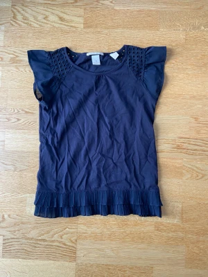 Volangtröja - Säljer denna t-shirt med volangdetaljer i ärmarna och längst ner. Säljer då den är för liten för mig. Storlek xs/s. Säljer för 80kr+frakt.