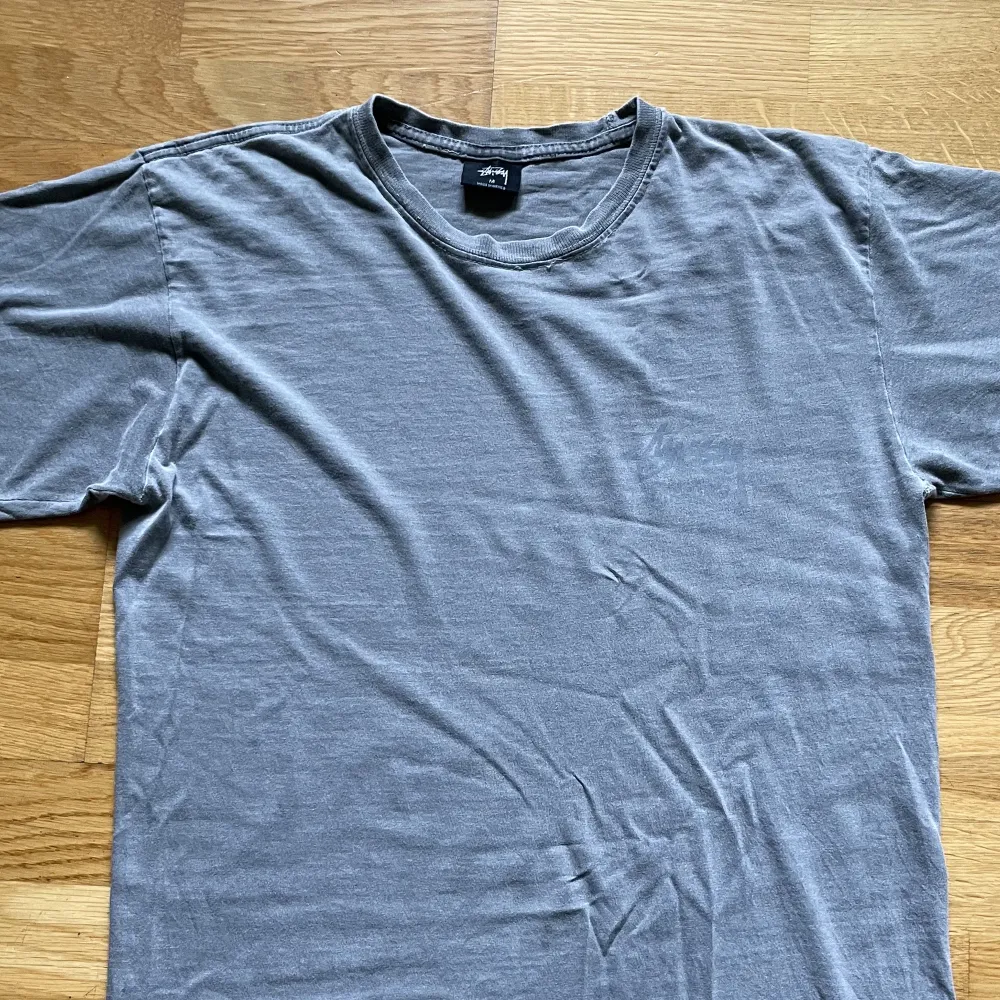 Gråtvättad Stüssy pigment dyed tshirt vilket ger vintage look. Motiv på baksida, stüssy logga på bröstet.  Tag säger M men passar som S. T-shirts.