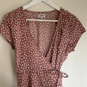 Sommar klänning - En fin kortärmad sommarklänning med knytning i midjan som fångar upp kroppens figur. Färgen är gammalrosa med vita prickar. Längden är vid låten på mig som är 175cm lång. 