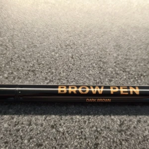 Anastasia Ögonbrynspenna - Mörkbrun - Brow Pen från Anastasia Beverly Hills är en penna med en hårfin spets som är idealisk för att skapa realistiska ögonbrynsstreck och ögonbryn med det mest naturliga utseendet någonsin. Färg: Dark Brown