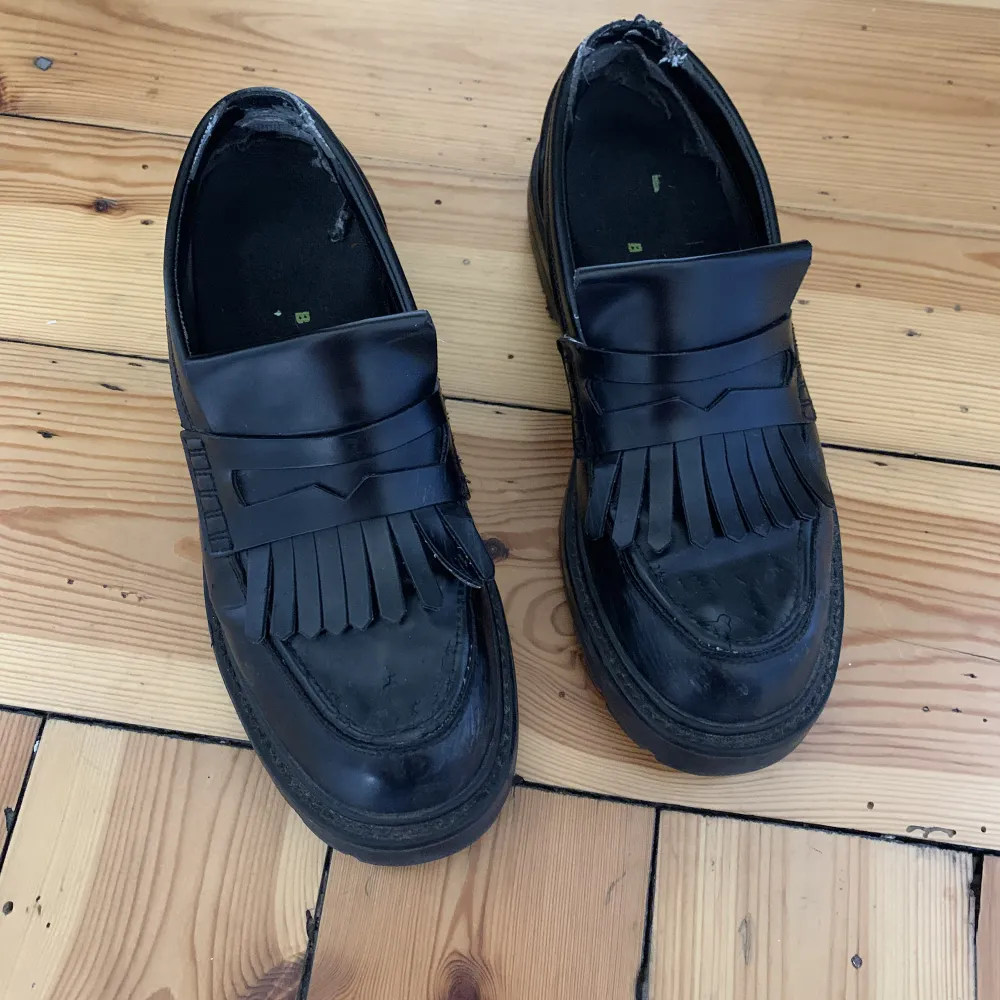 Black faux leather loafers with a small platform and fringe  . Skor.
