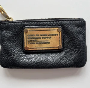 Marc Jacobs plånbok - Plånbok/nyckelplånbok från Marc Jacobs i använt skick. Märket och spännet på dragkedjan är lite slitet men annars i fullt gott skick! Kostade 1299kr ny, säljer den för 180