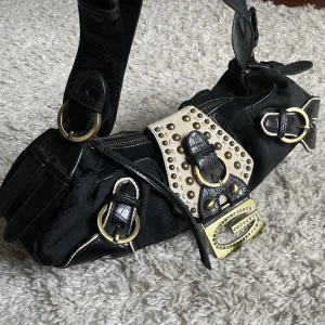 Vintage Guess väska - Vintage Guess väska. ❤️ Går att ha som axelväska eller handväska. Guld och svart, har flera snygga detaljer och mönster. En del rhinestones saknas från G:t. 🫶 Håll utkik på min profil, säljer för det mesta vintage kläder. 😍