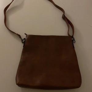 Brun axelremsväska  - Oanvänd axelremsväska i oäkta skinn.  Används inte p ga för liten storlek. 