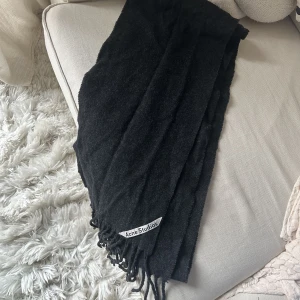 Mörkgrå Acne halsduk i ull - Mörkgrå Acne halsduk i ull (FRINGE WOOL SCARF - SKINNY). Sparsamt använd så fint skick. Längre och något smalare i modellen. Sista bild är modellen men ny kollektion och ljusare grå