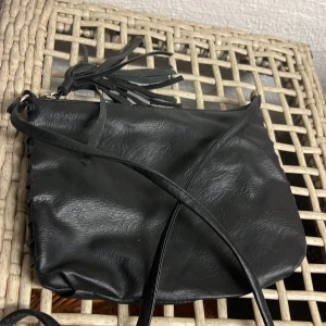 Axelremsväska  - Liten axelremsväska med fina detaljer. Ett litet dragkedjefack inuti och hela väskan stängs med en till dragkedja 