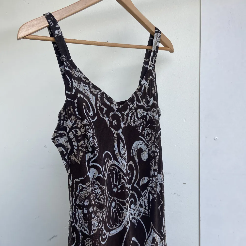 Mörkbrun mönstrad klänning med mönster längs benen. Klänningar.