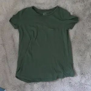 En grön T-shirt med en fake ficka över det vänstra bröstet. Tröjan är i väldigt bra skick då jag har använt den ett fåtal gånger. 