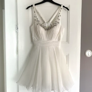 Vit fest/studentklänning  - Vit klänning med stenar över bröst och axelband. Dold dragkedja i ryggen och inbyggda kupor i bröstpartiet. En Sten har trillat ur fästet på baksidan av axelbandet (se bild 3), men inget som syns vid användning. Använd 1 gång. Storlek XS-S, finns i Malmö. 