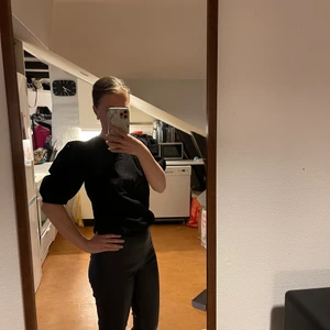 Svart topp/blus med puffärmar från NELLY, NLY TREND, Storlek 34 - En svart topp/blus med puffärmar från NLY TREND. Knappar i ryggen för en cool detalj. Helt oanvänd. Nyskick. Storlek 34.