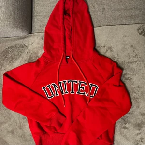 Röd hoddie, kroppad - En kroppad röd hoodie med vit svart text. Storlek s och är medel kort. Inte lång och inte kort. Slutar ungefär vid höften/ nedre magen