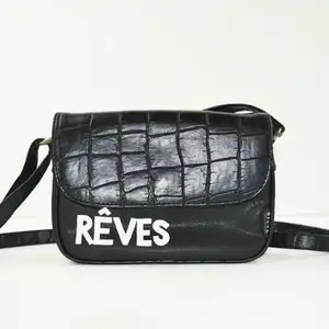 En svart basic väska med skinndetaljer och vita bokstäver nedtill. Lång axelrem som går att justera. ”Rêves” betyder  drömmar på franska. 