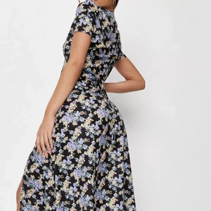 Blommig klänning - Total oanvänd klänning med blommigtryck med detaljer i halvknappen, mager knytbälte och delad sidofåll. Framhäver ens naturliga former. Materialet är i polyester.                                                 