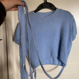 Blå stickad topp - Säljer denna fina blå stickade toppen med snörning runt magen som blir skitsnyggt! Säljs för den ej används, bara använt 2 gånger så i nyskick. Från collusion. Skickar spårbart endast om det önskas!