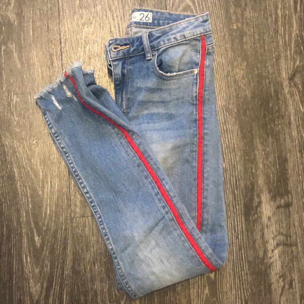 Blåa jeans med rött streck på sidan på båda benen. Hål i en knät. Storlek 26. Kostar 70kr + frakt om du inte kan mötas. Jeans & Byxor.