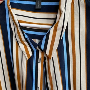 Skjorta  - Randig skjorta i vitt, ljus blått, mörk blått och rostfärgad. Längre modell, snygg som oversized eller som en öppen skjorta att ha över. 