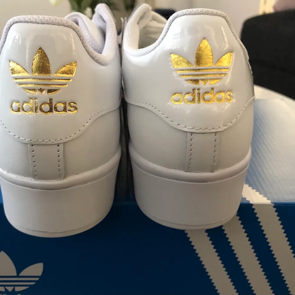 Ett par vita adidas sneakers med guld detaljer och glansiga stripes på sidorna. Använd 2 gånger, inprincip nya. Strl 39 1/3 - säljer pga för stor storlek. . Skor.