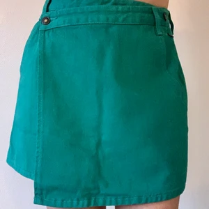 Kjol storlek M - Smaragdgrön omlottkjol med fickor och svart knappar, lite styvare bomullsmaterial (typ som en jeanskjol), från Shein, använd en gång, midja: 71cm, längd bak: 39cm 