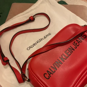Ck röd väska  - Calvin Klein röd väska som jag använt flertal gånger men är fortfarande i fint skick. De är röd och svart text och man får en dustbag påse med. Köpte den i originalpris i Finland för 1200kr och mitt pris är 400kr