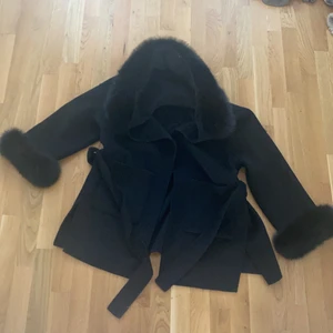 Kappa med äkta päls.  - Ullkappa som har en blandning av ull och  cashmere.  Kappan har en stor luva med äkta päls och 2 ”tofsar” precis vid armarna. Avtagbar luva och dem 2 små tofsarna. Kappan knäpps omlott med ett band. Även 2 stora fickor. Strl XS, men kan användas till S - M för den är  oversized. Knappt använd. Mer information o bilder om ni vill. Priset kan också diskuteras. Frakten ingår inte
