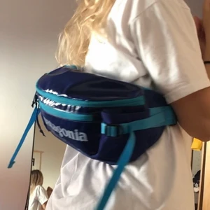 Patagonia midjeväska 5l - Patagonia Black Hole Waist Pack 5l cobalt blue. Blå midjeväska med rymliga stretch-fickor och justerbart midjeband. Baksidan är i mesh för att få bättre ventilation och komfort när du bär den.  I fint skick bortsett från några mindre slitningar på baksidan (som ej syns när man har den på sig och som ej stör funktionen), något smutsig på bandet samt mindre slitningar på märket framtill, Se bilder för egen bedömning. Kan skicka fler bilder. 