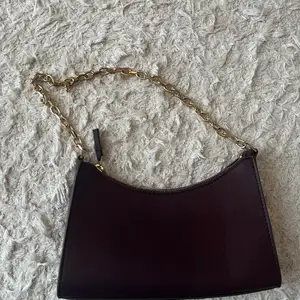 En snygg, liten och mörkröd handväska från Mango med guldkedja. 