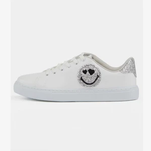 Skor - Säljer ett par vita sneakers med en smiley. Helt oanvända. Säljer dem pågrund av att de är för små. Jättebra till sommaren.