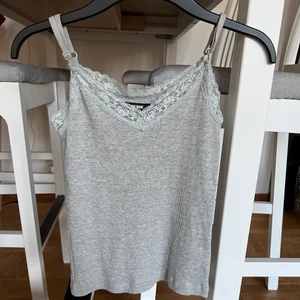 Gulligt linne med spetsdetaljer - Ett grått, ribbat linne med spetsdetaljer. Linnet är endast använd 2 gånger så i fint skick!