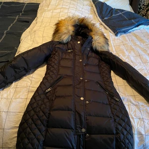 rock and blue jacka - Svart dunjacka med avtagbar huva och konstgjord päls. Fina quiltade delar på sidorna. Dragkedja och knappar framtill. Två sidofickor som stängs med dragkedja. Logotyplapp och ficka med dragkedja på ena ärmen. Säljer den pågrund av att jag köpte för liten storlek.