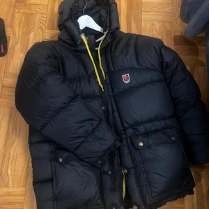 Äkta fjällräven dunjacka strl XS  - Fjällräven dunjacka i den populära färgen blå/grå. Mkt fint skick! Nypris strax över 6000kr. Strl XS men stor i storleken, såsom de är. Har passat mig som är ca strl 38. — obs! 3 små förstärkningslappar som knappt syns (se bild 2), en på ryggen och två under armarna (ca 1 cm vardera). ——- Kan behöva torkas av/tvättas lite smått (små stänk här och där från vädret) men jag vågar inte köra den i tvättmaskinen, bättre att den som köper gör det :) KÖPARE STÅR FÖR FRAKT! 