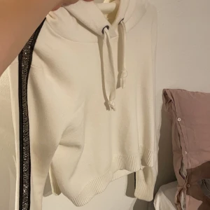 Stickad hoodie med detalj - Stickad hoodie som är kortare i modellen. Har fina detaljer på armarna där det är som paljetter eller glitter eller vad man kan kalla det. Köparen står för frakt. Storlek medium med passar bra på XS/S