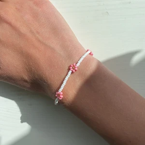 Armband med blommor🌸✨ - Armband med vita pärlor och små rosa blommor med guld pärla i mitten. Gjort på elastikstråd, passar alla! Frakt tillkommer. Hör av dig vid frågor💖💗💞