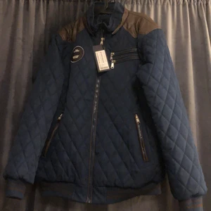 Herr vinter jacka - Oanvänd vinterjacka köpt för 599kr, prislappen sitter kvar, säljs för 300kr. Storleken är XXL. Färgen på jackan är marinblå med bruna skinndetaljer. 