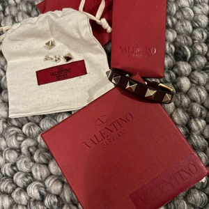 Valentino armband  - Säljer mitt vinröda Valentino armband med Rosenlund detaljer. Det som är skadan är att armbandet där bak har splittras i 2 och det är bara att limma ihop så syns det ej. Allt som ni ser på bilden ingår