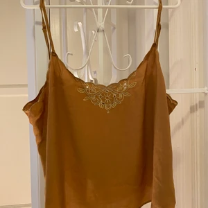 Bronztopp med guldbroderingar - En tunn topp i bronz/orange/brunt med guldiga detaljer. Storlek s. Pris exklusive frakt. 