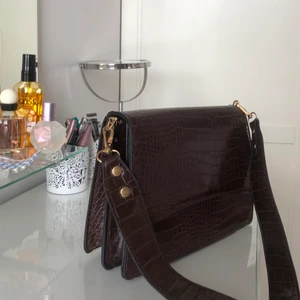  Brun väska - Brun handväska köpt på second hand :) otroligt fint skick och knappt använd, den låser sig när man stänger den och trcker in en knapp så öppnar den sig. Man får med två axelband vid köpet :) den är 22 cm bredd och 16 cm djup:)