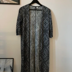 Lång tunn cardigan  - En jättefin cardigan från hm med vita och svarta mönster på. På mig går den ner till knävecken ungefär och jag är 170cm. Länst ner så har den ca 10cm slits på vardera sida. Ärmarna går strax nedanför armbågarna. Tunnt material, storlek S✨