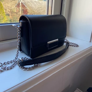 Väska  - Säljer denna svarta väskan som är köpt på accent. Mycket bra skick förutom att kedja att tappt lite färg på vissa ställen inget som syns om man inte kollar noga. Ungefärliga mått: 18x12x6cm. Kedjans längd: 110cm. Startpris 100kr