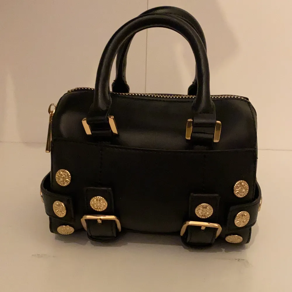 En mindre svart bowler väska med guld detaljer från Topshop. Det finns ett ytterfack, samt en korthållare i huvudfacket. Är i topp skick! B:14L:20H:14 (cm). Laukut & Käsilaukut.