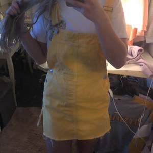 En gul kort klänning med två band som man kan justera längden på, finns även fickor.