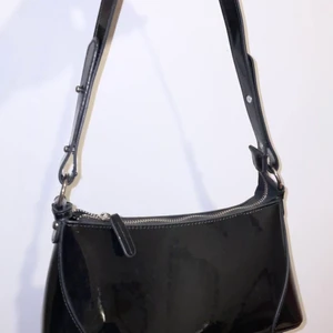 Svart axelväska - En svart väska som glänser i nytt skick. Inget fel på den, fick väskan som present och har i princip aldrig använt den förutom några gånger. Frågor och pris kan diskuteras 🤍