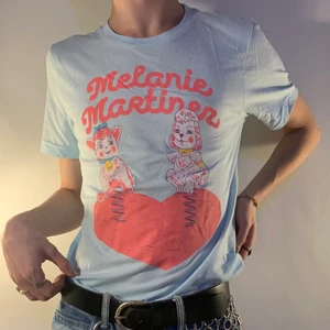 Melanie Martinez merch t-shirt k-12 blå  - Baby blå Melanie Martinez graphic tee med rosa tryck av två gunghästar på en lekplats 🎠 Jag köpte denna tröjan på hennes konsert i februari 2020 och är nästintill oanvänd vilket gör att kvalitén är drömlik! Verkligen så skön! T-shirten är perfekt till att bara chilla i hemma men också til ett par blåa jeans för att komplettera det blåa i t-shirten! Men ännu coolare med ett par rosa eller gula byxor för att klä upp det och matcha med färgerna i tröjan!