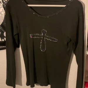 Tröja med paljetter - Grön tröja med paljetter och pärlor på som formar, vad jag tolkar det som, ett kors. Skitsnygg och passar perfekt till en lite fairy grungig outfit! Endast använd en gång av mig men köpt secondhand 