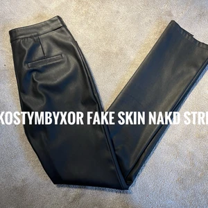 FAKE SKINBYXOR FRÅN NAKD STRL 36 - Byxor i fakeskin från NAKD i strl 36. Är väldigt stretchiga så passar större storlekar, brukar själv ha 38-40 och passar på mig. Är i kostymbyxor modell men i fake skin. Har slits nedtill och dekorativa fickor bak. Är höga i midjan och skinny fit i benen men blir luftiga nedtill pga slitsen. Jag är ca 170 och dom slutar vid ankeln på mig. Är lite slitna i knappen annars i bra skick. Kan skickas (frakt tillkommer) eller mötas upp i centrala Uppsala.