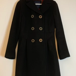 Svart GANT Ullkappa i storlek S - Superfin svart figursydd ullkappa från GANT med rödrutig foder och 6 bröstknappar. Storlek S, fint skick, inga skavanker! 