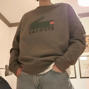 Lacoste Grå Collegetröja  - Säljer min "mörk" Gråa Lacoste Collegetröja med logga samt texten "LACOSTE" på. Herr modell storlek XL. Säljs på grund av att den inte kommer till användning tyvärr, men den är riktigt snygg! (DMa för mer bilder)