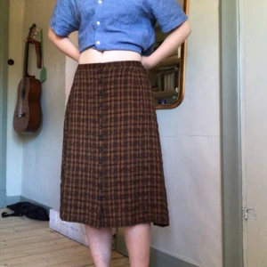 Brun kjol!  - Brun-rutig kjol med knappar från Lindex som jag har sytt in och upp för att passa bättre. Väldigt bra skick! Midjemått: 70cm men det finns stretch i bak. Längd: 63cm. Troligtsvis från 90talet eller 00talet. Kolla gärna in mina andra anonnser, samfraktar vid köp av två eller fler varor🍀