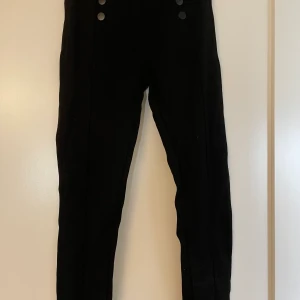 Kostymbyxor  - Svarta kostymbyxor med knappar. Sen har dom även en söm fram på benen 